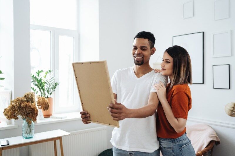 A happy couple stares at a picture of their family while hanging photo frames and creating a family photo wall